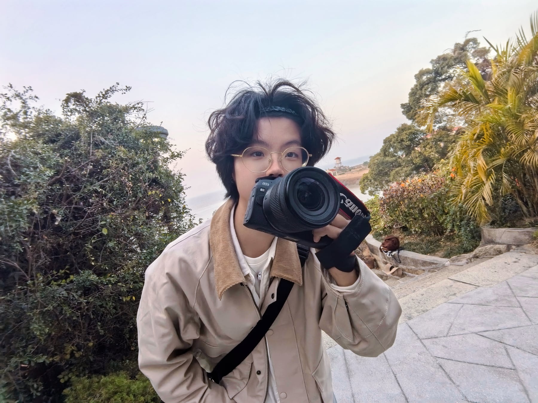Rayce Zhang outdoors holding a camera, with trees in the background.