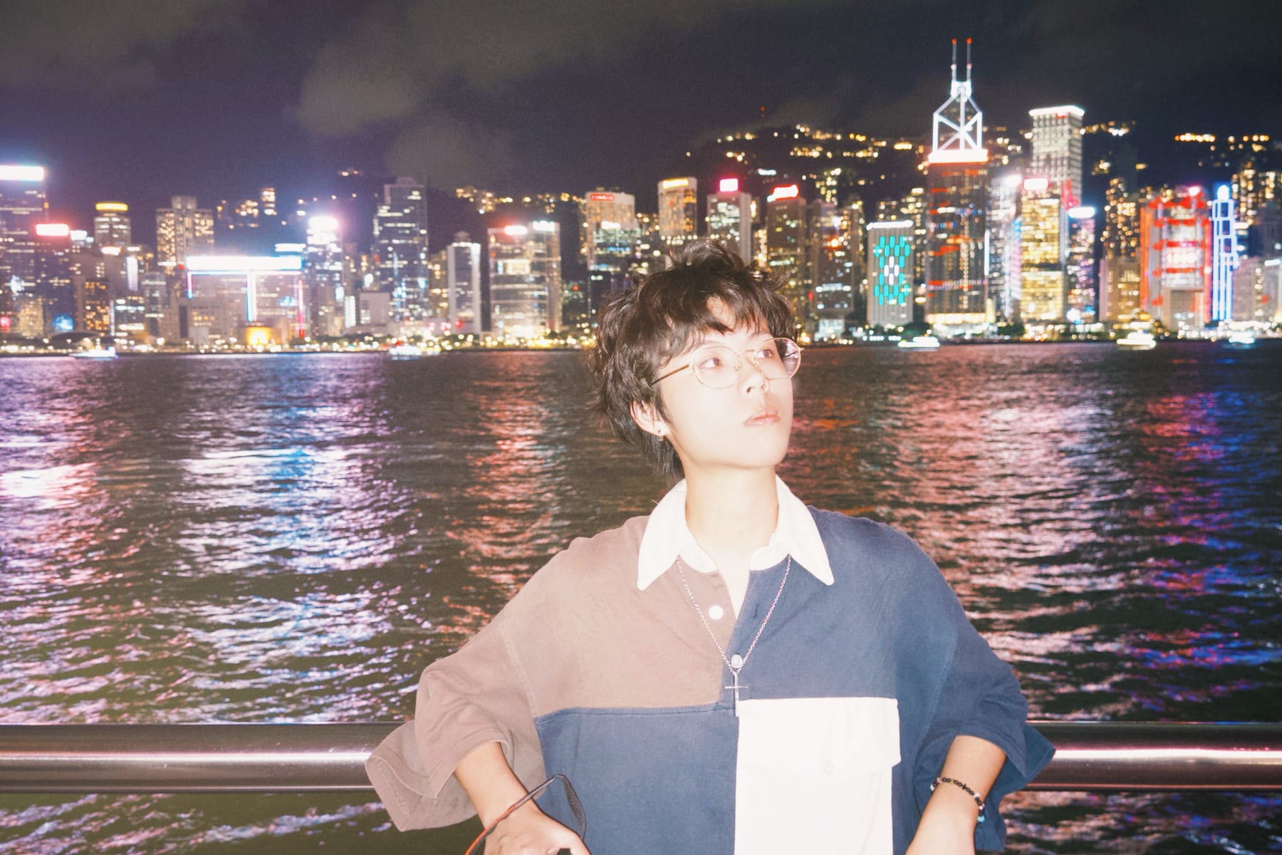 Rayce Zhang beside the harbour with an illuminated skyline at night.