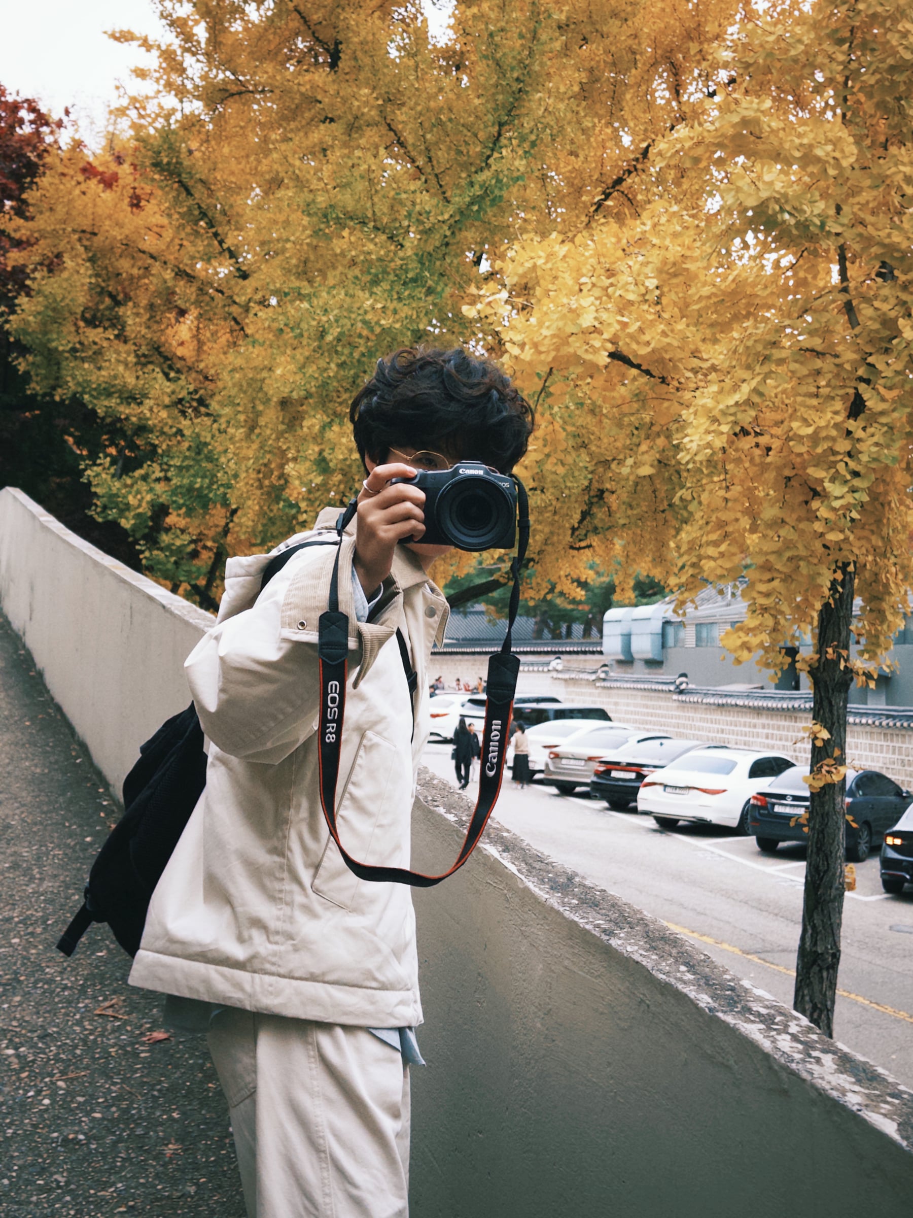 Rayce Zhang holding a camera beneath golden autumn leaves.